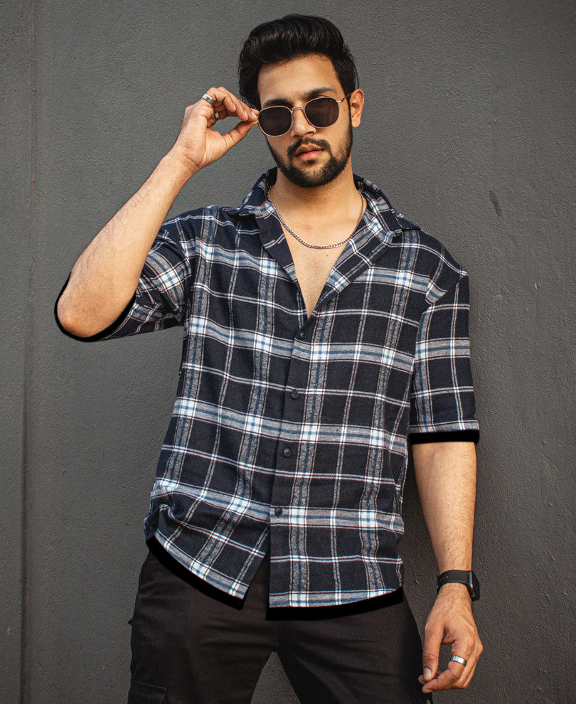 A man wearing a Navy Blue Checked Print Shirt and Black Bottom, giving a pose while holding his glares.